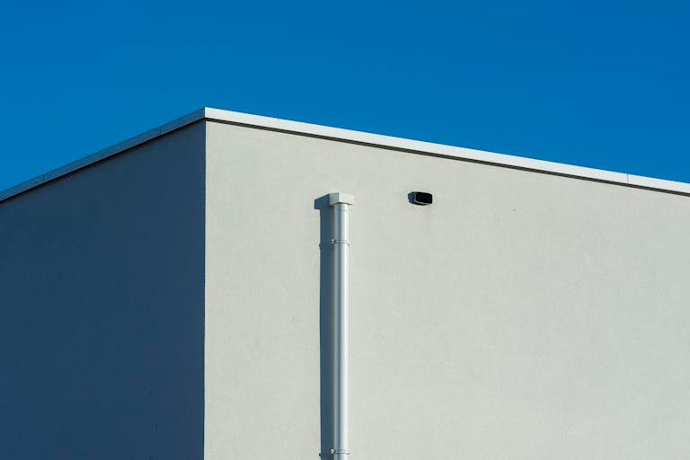 A minimalist architectural shot featuring a sunlit building corner against a clear blue sky.