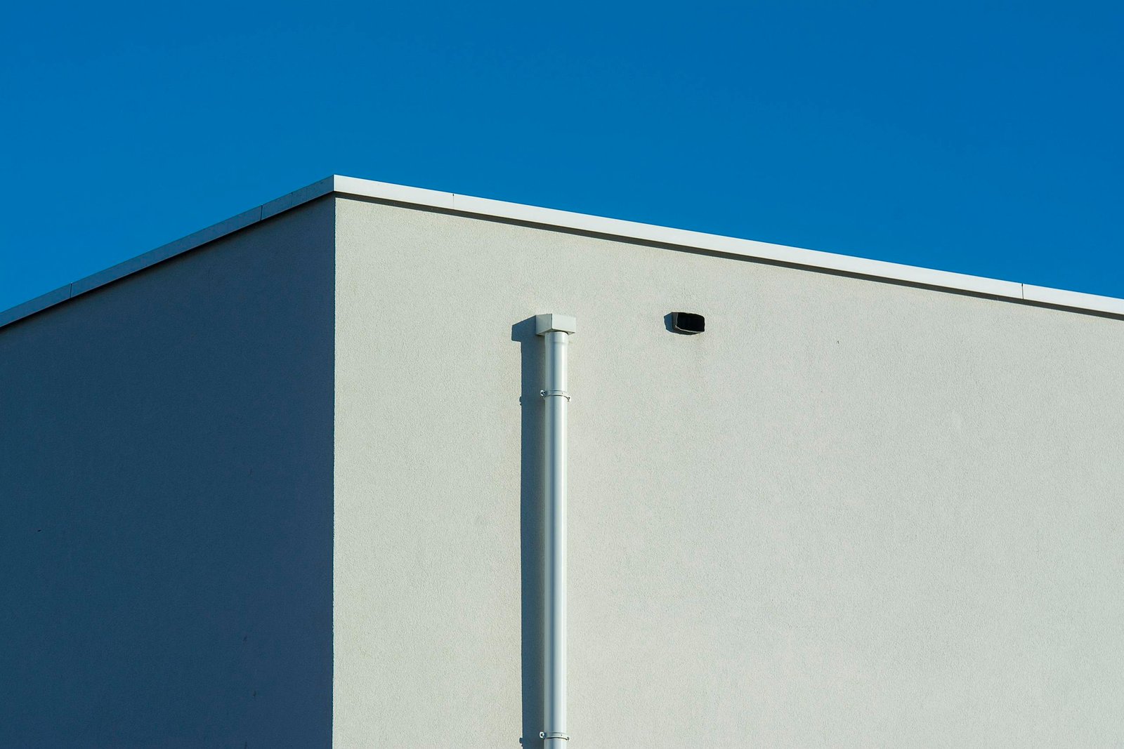 A minimalist architectural shot featuring a sunlit building corner against a clear blue sky.