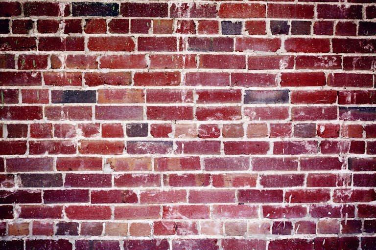 Close-up of a red brick wall showing its weathered texture and intricate pattern.